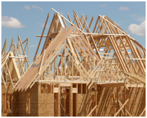 A construction site featuring wooden frames and roof trusses against a blue sky.