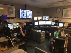 A busy control room with multiple monitors, a clock, and personnel managing operations.