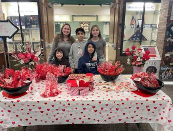teens gathered for photo at a desk filled with valentines flowers and chocolates