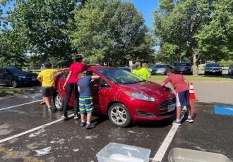 kids washing a red car in a parking lot