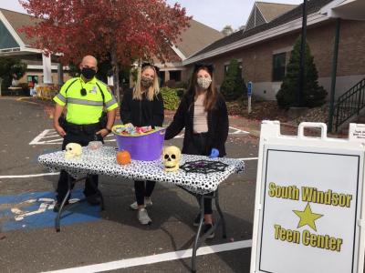 people standing in parking lot with hallowenen candy at a table next to a sign that says south windsor teen center