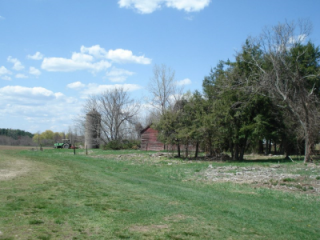 A rural landscape featuring green grass, trees, and a red barn under a blue sky with scattered clouds.