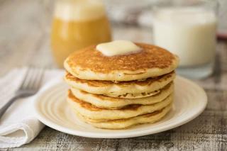 White plate with five golden pancakes topped with syrup and a pad of butter